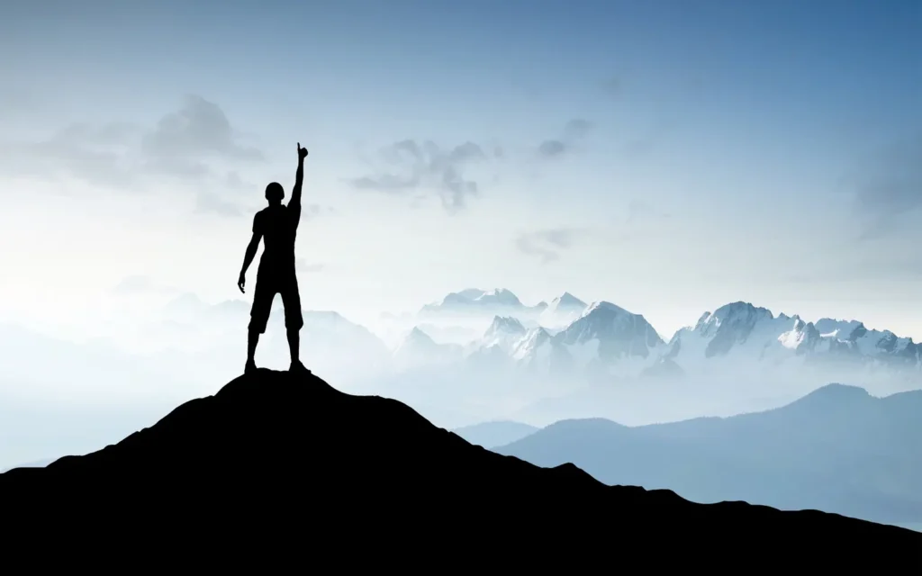 Person auf einem Berggipfel mit Blick auf eine weitläufige Landschaft